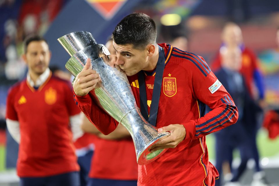  Alvaro Morata, wearing a red jersey with the word 'Spain' on it, kisses the trophy after winning the 2022 UEFA Nations League.
